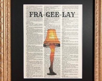 May include: A framed print of a dictionary page with the word "fragile" highlighted. The word is surrounded by a red and yellow lampshade with a woman's legs and feet visible. The lampshade is a popular Christmas decoration.