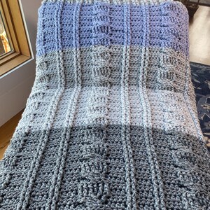 May include: A crocheted blanket with a textured pattern in shades of gray and purple.