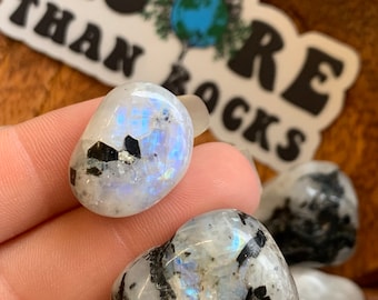 May include: Two tumbled moonstone crystals with black inclusions. The crystals are heart-shaped and have a white, iridescent sheen.