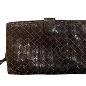 May include: A dark brown rectangular wallet featuring an intricate woven leather pattern across the entire surface. The wallet includes a central snap-button closure tab at the top edge and a small zip pull detail visible on the left side.