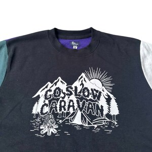 Puede incluir: Sudadera negra con un gr&aacute;fico blanco de una cordillera y el texto "Go Slow Caravan". La sudadera tiene paneles de color verde y gris en las mangas.