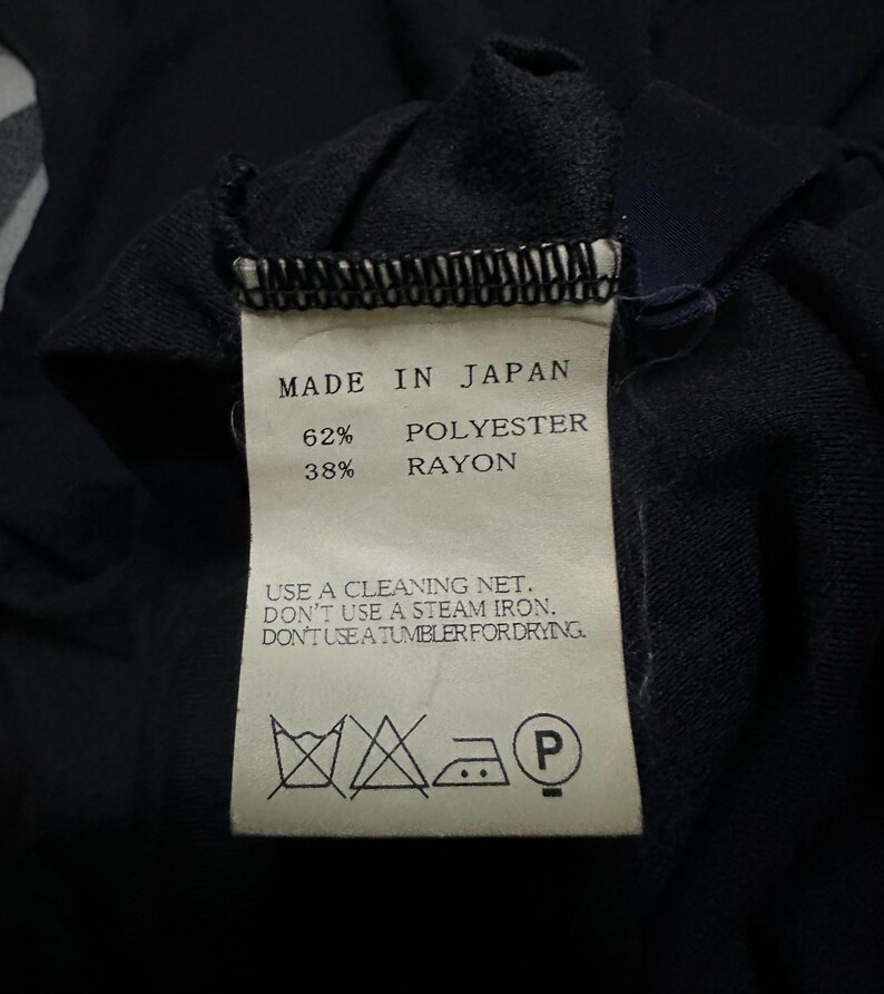 K&ouml;nnte beinhalten: Nahaufnahme eines Etiketts mit der Aufschrift "MADE IN JAPAN", Stoffzusammensetzung: 62% Polyester, 38% Rayon. Pflegehinweise: Reinigungsnetz verwenden, kein Dampfb&uuml;geleisen, nicht im Trockner trocknen.