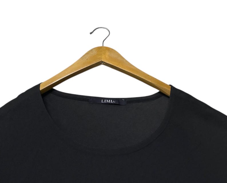 K&ouml;nnte beinhalten: Ein schwarzes Oberteil mit Rundhalsausschnitt, das an einem Holzkleiderb&uuml;gel h&auml;ngt. Das Oberteil hat ein schlichtes, minimalistisches Design. Der Markenname "LIMI" ist auf einem kleinen Etikett am Ausschnitt zu sehen.