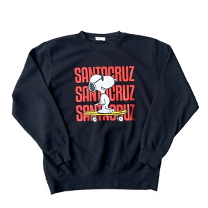 May include: Black sweatshirt with a red "Santa Cruz" logo and a cartoon image of Snoopy wearing sunglasses and riding a skateboard.