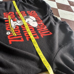 May include: Black long-sleeve sweatshirt with a red graphic of Snoopy riding a skateboard and the text "Santa Cruz" in red.