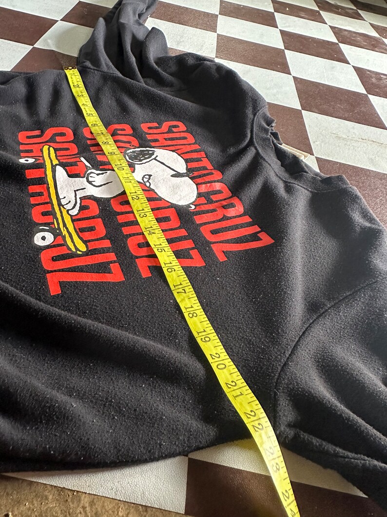 May include: Black long-sleeve sweatshirt with a red graphic of Snoopy riding a skateboard and the text "Santa Cruz" in red.