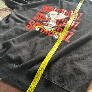 May include: Black sweatshirt with a graphic of Snoopy skateboarding and the text "Santa Cruz" repeated three times.