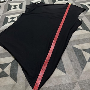 K&ouml;nnte beinhalten: Ein schwarzes, &auml;rmelloses Oberteil mit asymmetrischem Saum. Ein rotes Ma&szlig;band zeigt eine L&auml;nge von etwa 84 cm. Das Oberteil hat einen Rundhalsausschnitt und ein schlichtes, minimalistisches Design.