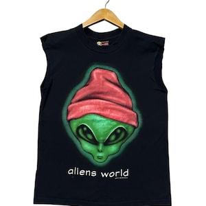 May include: Black sleeveless t-shirt featuring a green alien head wearing a red beanie. The alien has large black eyes and a small mouth. The words "aliens world" are printed in white below the alien's face.