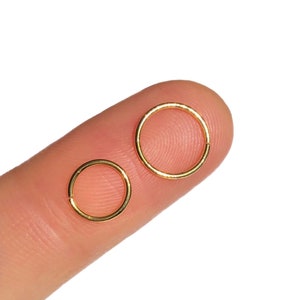 Könnte beinhalten: Zwei goldfarbene Creolen, eine größer und eine kleiner, werden auf einem Finger gezeigt.