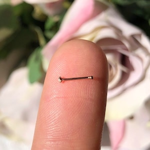 Op de afbeelding: Een neusring van roségoud met een kleine bol aan elk uiteinde.