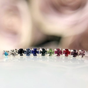 May include: A silver ring with a row of colorful gemstones. The stones are turquoise, white, black, blue, dark blue, green, red, purple, and light purple.