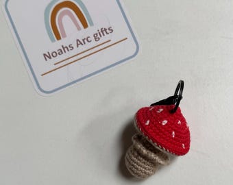 May include: A crocheted mushroom keychain with a red cap and white dots, a brown stem, and a black metal ring.