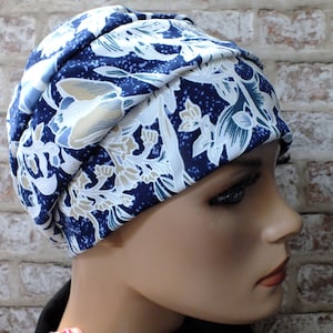 May include: A blue and white floral patterned turban style hat. The hat is made of a soft, stretchy fabric and has a gathered look.