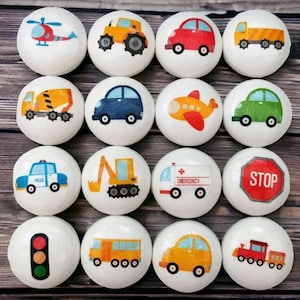 May include: Set of 12 white round wooden ornaments with various transportation themed designs. The designs include a helicopter, a yellow truck, a red car, a cement mixer, a blue car, a plane, a green car, a police car, a construction vehicle, an ambulance, a stop sign, a traffic light, a yellow school bus, a yellow car, and a train.