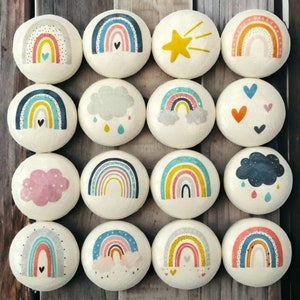May include: Twelve round wooden decorations featuring a variety of designs, including rainbows, clouds, stars, and hearts. The decorations are painted in pastel colours and have a white background.