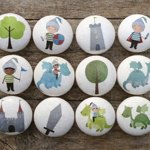 May include: A set of twelve white cabinet knobs, each with a unique design. The illustrations include trees, castles, knights, dragons, and swords. These decorative knobs are ideal for adding a playful touch to furniture or decor.