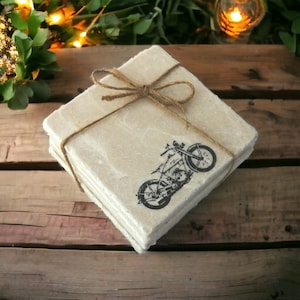May include: Set of four beige stone coasters featuring a vintage motorcycle design. The coasters are tied together with twine.
