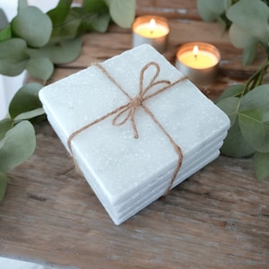 May include: Set of four white marble coasters tied together with twine. The coasters have a speckled, textured surface.