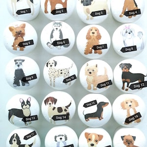 May include: A set of twenty round white wooden cabinet knobs, each featuring a unique hand-painted dog illustration labeled with black tags from Dog 1 to Dog 20, showcasing various breeds including pugs, dalmatians, and dachshunds.