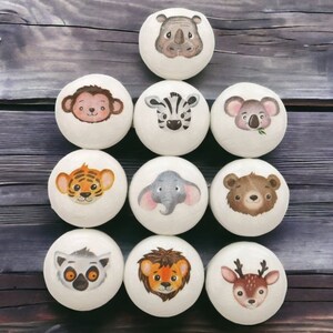 May include: Ten round, white, wooden ornaments with different animal faces painted on them. The animals include a monkey, zebra, koala, tiger, elephant, bear, lemur, lion, and deer.