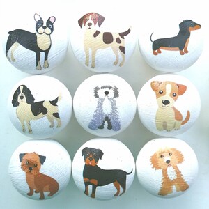May include: A set of nine round white wooden knobs, each featuring a different colorful illustration of a dog breed. The collection includes various canine figures such as a French Bulldog, a Dachshund, and a Rottweiler, all painted on a smooth surface.