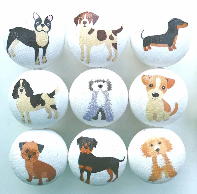 May include: A set of nine round white wooden knobs, each featuring a different colorful illustration of a dog breed. The collection includes various canine figures such as a French Bulldog, a Dachshund, and a Rottweiler, all painted on a smooth surface.