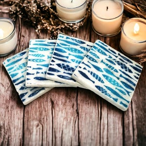 May include: Four blue and white ceramic coasters with a fish pattern. The coasters are stacked on top of each other on a wooden surface.