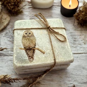 May include: Set of four white marble coasters with a brown owl illustration. The coasters are tied together with twine.