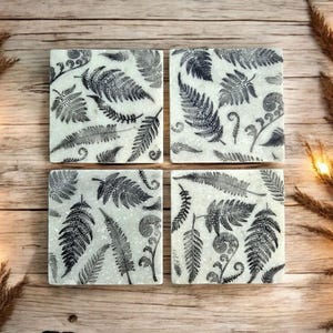 May include: Set of four white marble coasters with a black fern leaf design.