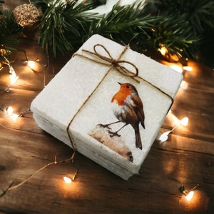 May include: A set of four white coasters featuring a robin design. The coasters are tied together with twine and have a rustic, farmhouse feel.