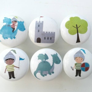 May include: Six white ceramic knobs with colourful illustrations of a knight, a dragon, a castle, and a tree. The knobs are approximately 3.8 cm in diameter.