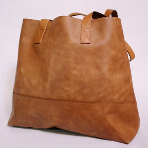 May include: A large, brown leather tote bag with a single, wide strap. The bag has a simple, minimalist design and is made of high-quality leather.