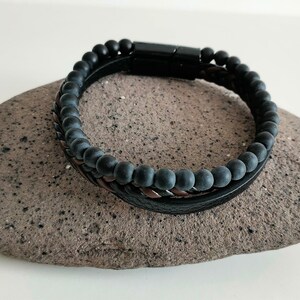 Op de afbeelding: Een zwarte kralen armband met een gevlochten leren band en een magneetsluiting.