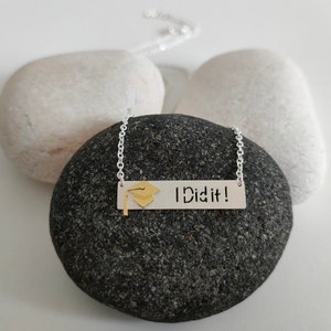 May include: Silver necklace with a silver bar pendant that says "I Did It!" and a gold graduation cap charm.