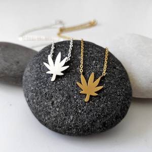 Peut inclure: Deux colliers en argent et en or avec un pendentif en forme de feuille de marijuana. Les colliers sont sur un fond gris et blanc.