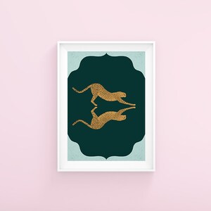 May include: A framed print with a dark green background and a light blue border. Two gold cheetah silhouettes are facing each other in a mirrored pose.