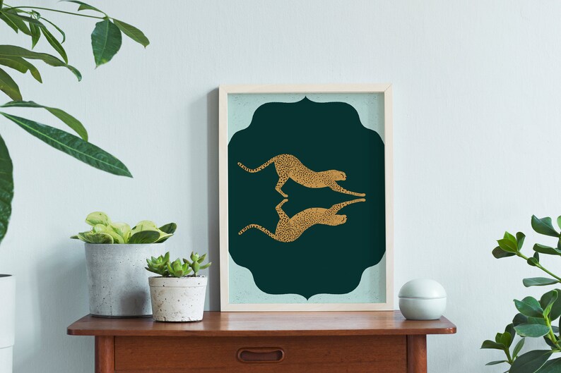 May include: A framed print with a teal green background and two gold cheetah silhouettes facing each other. The cheetah silhouettes are mirrored images of each other.