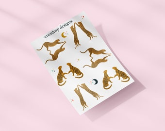 Puede incluir: Una hoja de papel blanco con ilustraciones de leopardos en silueta dorada en varias poses. El papel tiene el texto "eyesdrop designs." impreso en negro en la parte superior.