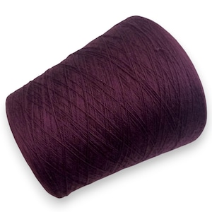 Puede incluir: Un gran cono de hilo morado oscuro, bien enrollado y listo para manualidades. El hilo tiene un ligero brillo, lo que sugiere una mezcla de fibras. El cono está sobre un fondo blanco, resaltando el rico color y la textura del hilo.