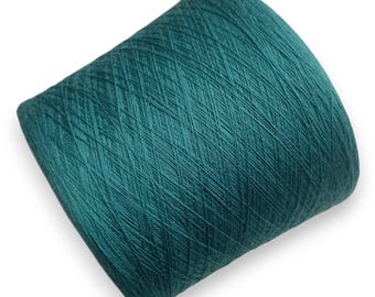 Puede incluir: Una bobina cilíndrica de hilo color verde azulado oscuro con un patrón de bobinado entrecruzado. El hilo está enrollado firmemente alrededor del núcleo central, creando una superficie texturizada con líneas diagonales visibles en toda la bobina.