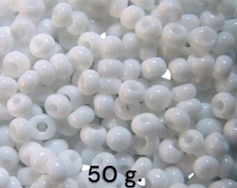 May include: A close-up shot of a pile of white, round beads. The beads have a hole through the center and a glossy finish. The text "50 g." is visible in the lower right corner. These beads are suitable for jewelry making and crafts.