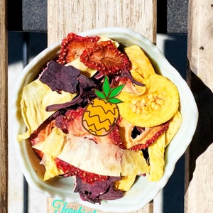 May include: A white bowl filled with a variety of dried fruits, including pineapple, strawberries, and mango. The fruits are a mix of red, yellow, and purple.