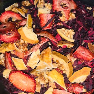 May include: A close-up of a bowl filled with dried fruit and flower petals. The fruit is a mix of red strawberries and light brown pieces of dried fruit. The flower petals are a deep red color.