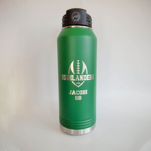 May include: Green stainless steel water bottle with a silver lid and a white engraved design. The design includes a football, the text "HIGHLANDERS 2021", and the name "JACOBI 68".