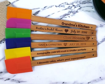 May include: Set of six colorful silicone spatulas with wooden handles. Each handle is engraved with a different message, including "Grandma's Kitchen", "Kristine's Bridal Shower", "Chef Monica", "Dave & Christina", "Annoying the cook will result in smaller portions", and "I decorate cakes, what's your superpower?"
