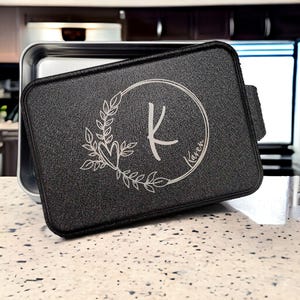 May include: Black metal baking pan with a removable lid. The lid has a silver engraved design of a wreath with a heart and the letter K inside a circle with the name Karen.