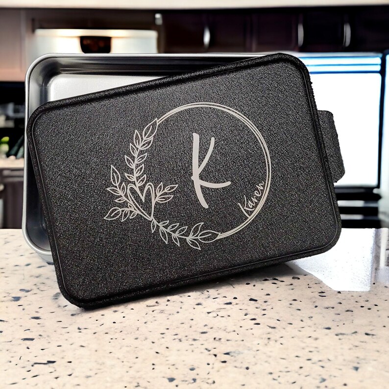 May include: Black metal baking pan with a removable lid. The lid has a silver engraved design of a wreath with a heart and the letter K inside a circle with the name Karen.