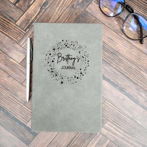 Peut inclure: Un journal en cuir gris avec un motif de flocons de neige noirs et le texte "Brittany's Journal" sur la couverture.