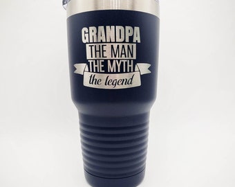 May include: A navy blue stainless steel tumbler with a silver lid. The tumbler has a white inscription that reads "Grandpa The Man The Myth The Legend".